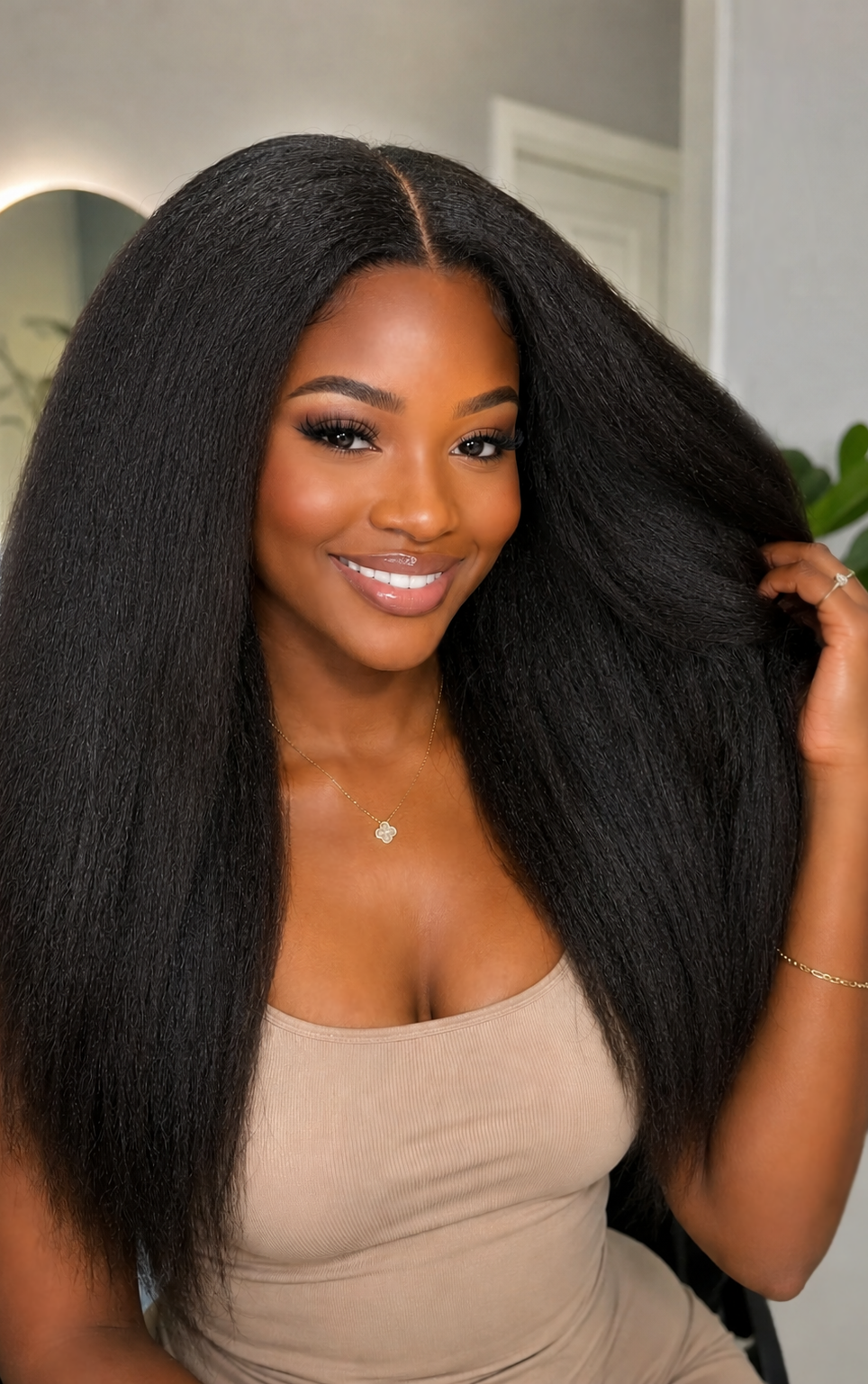 Woman with long, kinky straight black hair clips in wearing a beige top indoors.